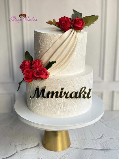 An elegant cake for a salon's grand opening. This two-tier design features a beautiful white-on-white stencil pattern and a graceful fondant drape, accented with classic red roses.