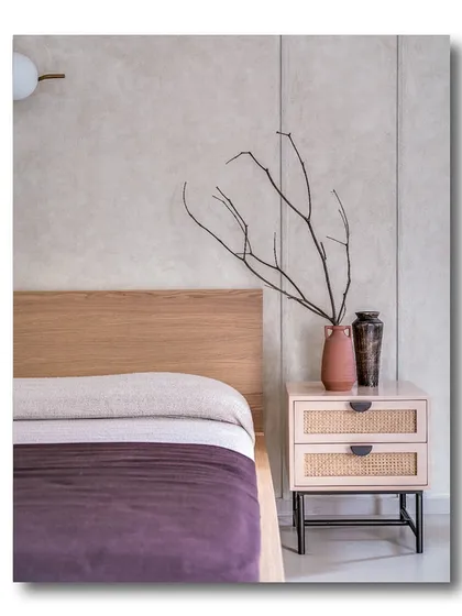 A minimalist bedroom corner where natural textures and a calm color palette reign. The light wood headboard, rattan-fronted nightstand, and simple dried branches create a serene and organic feel.