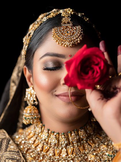 A creative shot of a bride with a red rose, highlighting the soft smokey eye makeup and flawless base. The focus is on the delicate details of the eye work and the overall romantic feel of the bridal look.