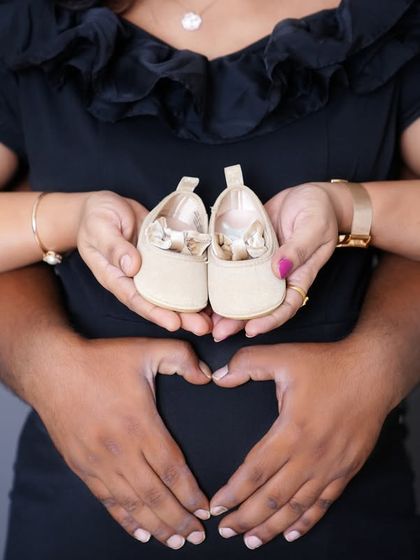 A creative maternity shot showing the couple's hands forming a heart on the baby bump, with tiny baby shoes held in front. It’s the little details that tell the biggest stories.