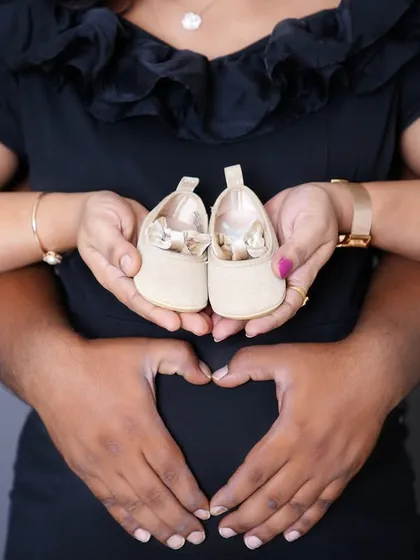 A creative maternity shot showing the couple's hands forming a heart on the baby bump, with tiny baby shoes held in front. It’s the little details that tell the biggest stories.