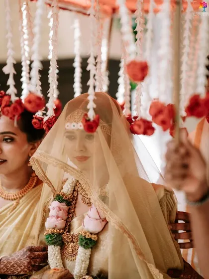 A beautiful shot of the bride under a sheer veil during her entrance. The hanging flowers add a delicate and traditional touch to this serene moment.