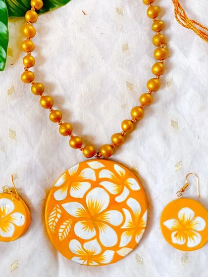 A bright and cheerful hand-painted floral pendant. The white flowers pop against the sunny yellow-orange background, making this a perfect accessory for summer.