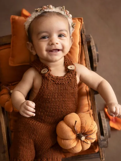 A bright, happy smile from the baby in her pumpkin-filled cart.