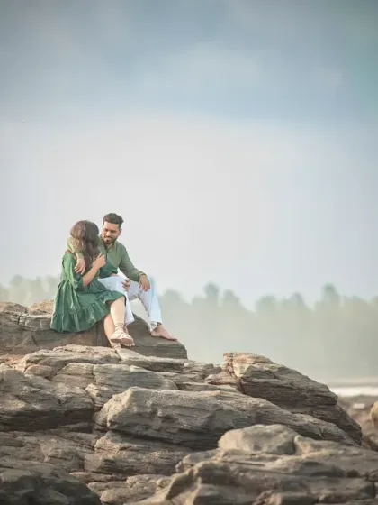 A wide, cinematic shot of a couple during their pre-wedding shoot. The dramatic landscape of the rocky shore adds a powerful and epic feel to their portrait.