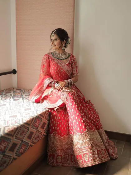 A full-length shot showcasing the complete bridal look. The soft, natural makeup perfectly balances the intricate details of her red lehenga and heavy jewelry, ensuring she looks like herself.