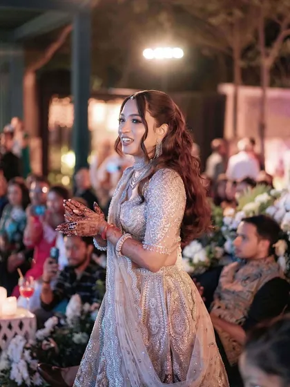The bride's joy is palpable in this photo. Her shimmering silver lehenga is paired with a glamorous makeup look that sparkles under the lights.