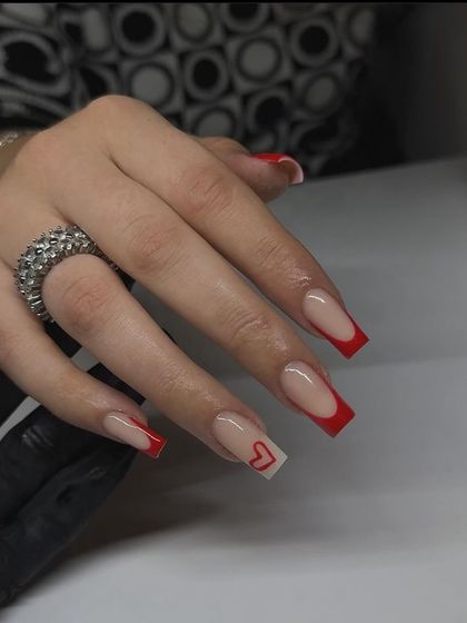 A modern red French manicure on long, square-tipped nails, with a single accent nail featuring a small, minimalist heart.