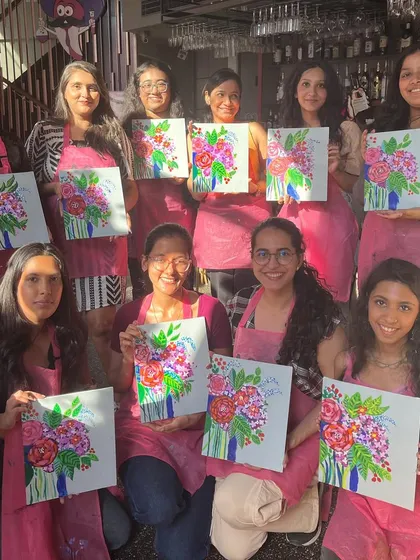 A group of participants holding up their floral abstract paintings at a cafe workshop. The bright colors and happy faces say it all.
