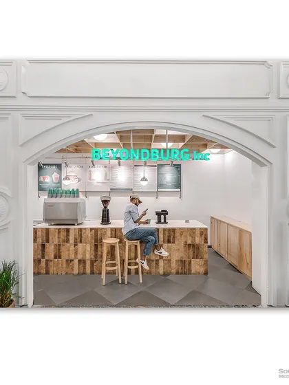 The storefront of "Beyondburg Inc," a modern cafe with a clean, minimalist aesthetic. The arched entrance and wooden counter create a warm and inviting first impression.