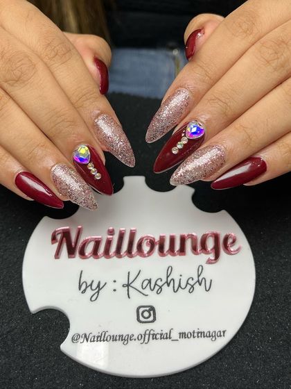 A bold maroon and silver glitter set on stiletto nails, with large iridescent rhinestones for extra drama.