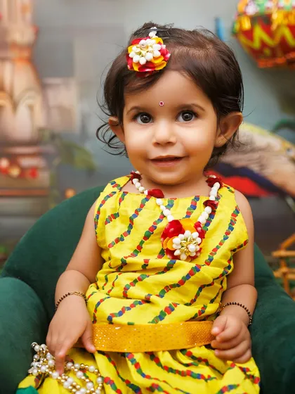 A sweet portrait of a little girl dressed as Radha, with a gentle smile and traditional jewelry.