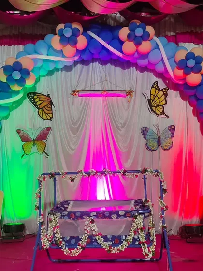 A colorful butterfly theme for a naming ceremony. The cradle is placed in front of a balloon arch with butterfly cutouts and dramatic lighting.