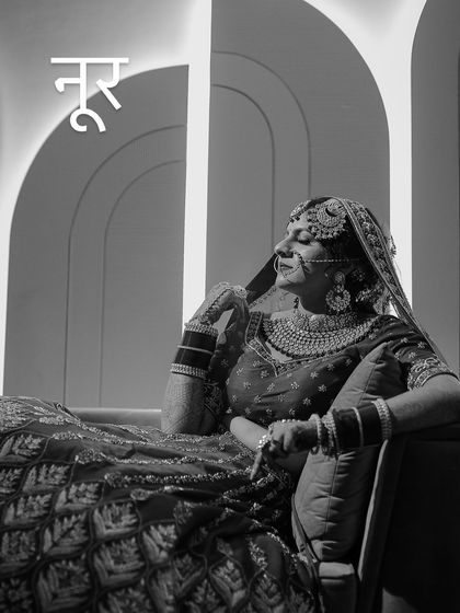 A black and white portrait of a bride resting on a sofa, with modern, linear lights in the background.
