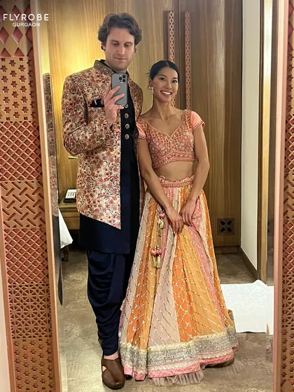 A happy couple taking a mirror selfie. Her vibrant multi-colored lehenga and his floral sherwani are a perfect match for a fun wedding event.