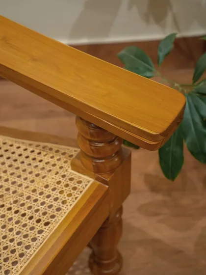 A close-up of the 'Orca' lounge chair, showing the junction of the turned leg, the sturdy armrest, and the handwoven rattan seat.