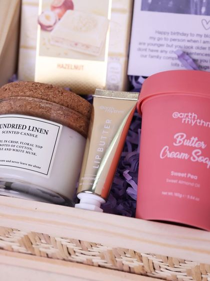 A close-up of the pampering items in the sister hamper, including a 'Sundried Linen' scented candle, lip butter, and 'Butter Cream Soap'.