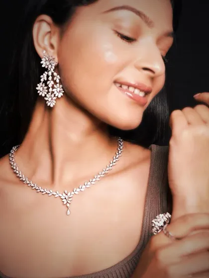 A model radiates joy while wearing a complete diamond set, including a leaf-pattern necklace, chandelier earrings, and matching rings.