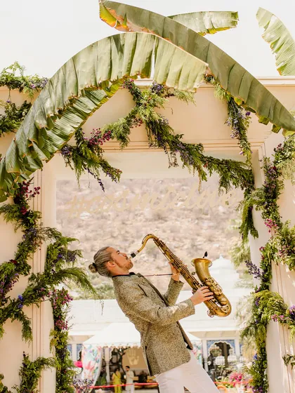 Live entertainment is key to a lively event. Here, a saxophonist serenades guests under an arch of banana leaves and florals, adding a touch of class and creating a wonderful ambiance.