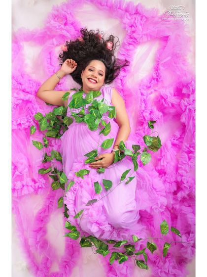 A joyful and creative top-down shot. The mom-to-be lies on a bed of pink tulle, adorned with green leaves, creating a unique portrait that feels like she's blooming.
