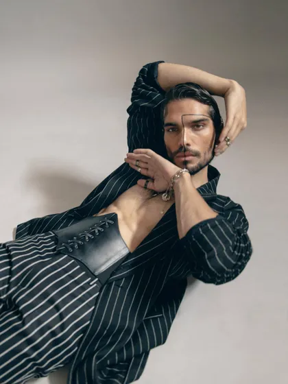 An angled shot showcasing the leather corset worn over an open pinstripe jacket. This image clearly displays the unconventional layering and androgynous styling of the look.