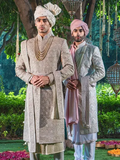 Two grooms stand together, showcasing complementary yet distinct sherwani designs. This illustrates our expertise in crafting coordinated looks for couples, ensuring each partner's style is honored.