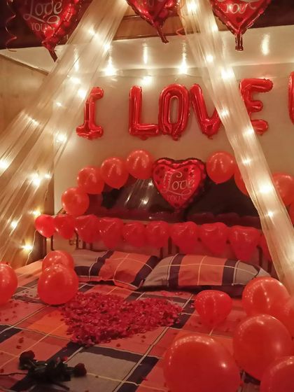 Lit by the soft glow of fairy lights, this romantic room setup is ready to create a beautiful memory. The "I LOVE YOU" balloons and heart-shaped petals on the bed make the intention clear and heartfelt.