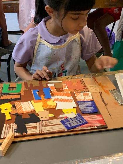 A student works on her Picasso-inspired collage, carefully arranging pre-cut shapes to form figures. This exercise teaches composition and abstract representation.