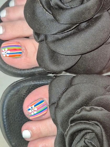 A chic pedicure with a mix of solid white polish and accent toes featuring colorful rainbow stripes and a delicate daisy.