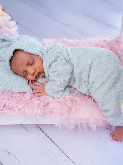 Sleeping soundly in a miniature bed, this newborn looks cozy and content in a fluffy blue sleeper. Floral accents add a soft, delicate touch.