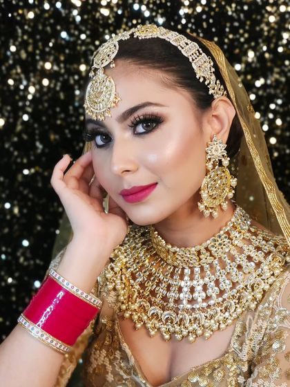 A beautiful bride wearing a heavy, champagne-gold bridal set with a matching matha patti and red choora.