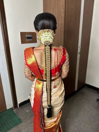 A full back view of a classic muhurtham look. The off-white saree with a red border is paired with a long braid and traditional temple jewellery.