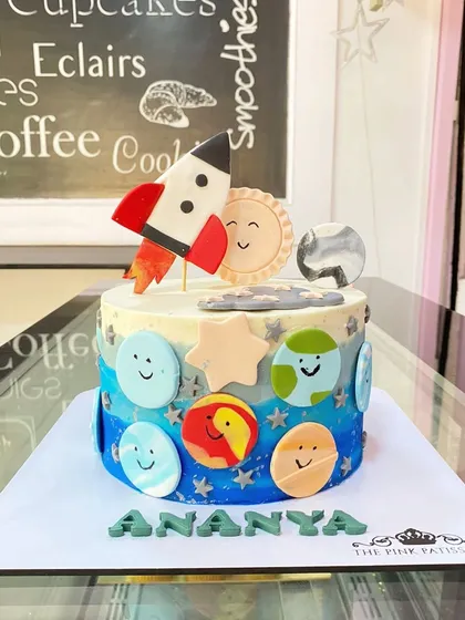 A cute and friendly planet-themed cake for Ananya, with smiling planet cookies and a rocket ship topper.
