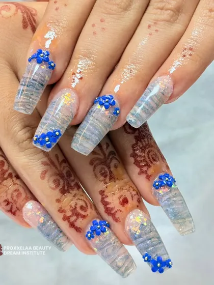 A closer view of the translucent wave design with 3D blue florals. You can see the subtle glitter embedded within the nail and the precise placement of each tiny flower.