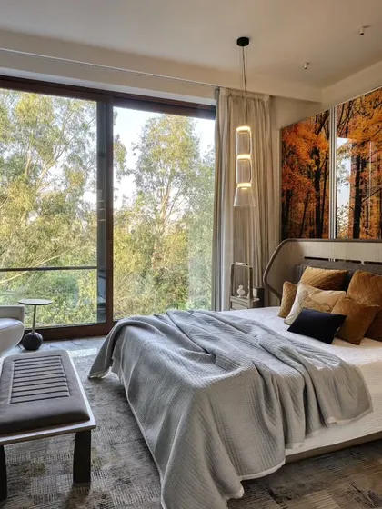 This contemporary bedroom brings the beauty of nature indoors with a stunning, autumn-themed wall panel. The large window offers a view of lush green trees, creating a beautiful contrast and a space that changes with the seasons.