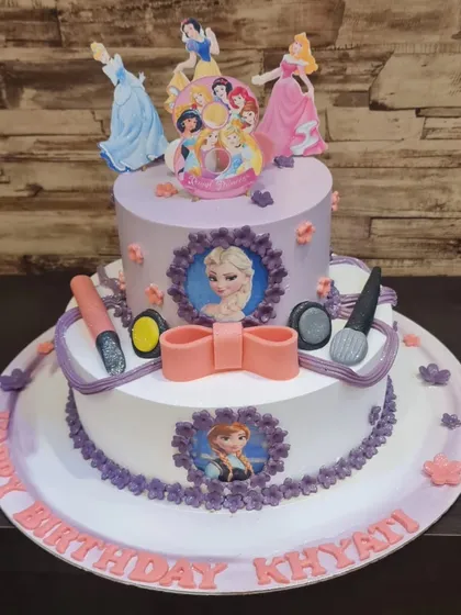 A royal two-tier cake for a true princess fan, combining the worlds of Disney Princesses and Frozen. This cake features characters like Elsa, Anna, and Cinderella, along with fun makeup-themed fondant details.