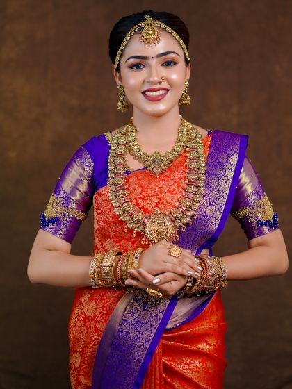 An orange and royal blue Kanchipuram saree styled for a photoshoot. The contrast is striking, and the drape is kept traditional to highlight the saree's grandeur.