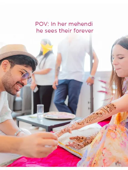 "In her mehendi, he sees their forever." A tender moment as the groom admires the intricate henna on his bride's hands.