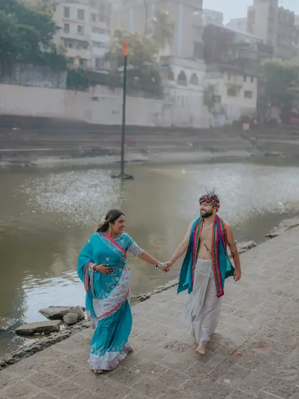 Walking along the ghats, hand in hand. This wide shot captures the couple in their beautiful traditional attire against the backdrop of the river and old city buildings.