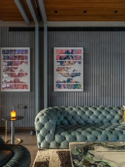 The living room features a tufted teal sofa set against a corrugated metal wall, a bold mix of industrial texture and luxurious comfort.