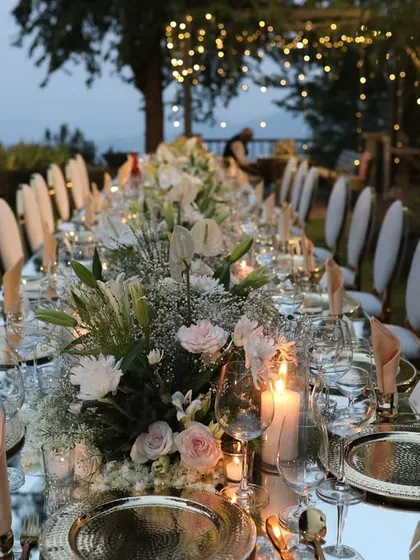 A long, mirrored dining table set for an elegant dinner. The continuous runner of white flowers and candles creates a stunning, cohesive look.
