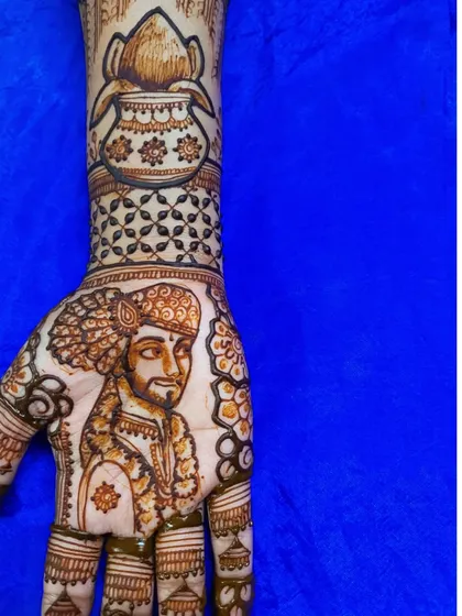 A detailed view of the groom's hand from a Maharashtrian bridal set. You can see the groom's portrait and a sacred 'kalash' pot, representing prosperity and blessings.