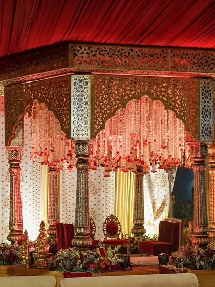 Another perspective of the royal mandap, highlighting the intricate jali work on the canopy and the grandeur of the carved pillars under a rich red draped ceiling.