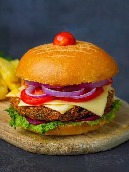 A delicious veggie burger with cheese, lettuce, tomato, and onion, served with fries on a wooden board. The dark, moody background is a classic choice for making burgers look epic.