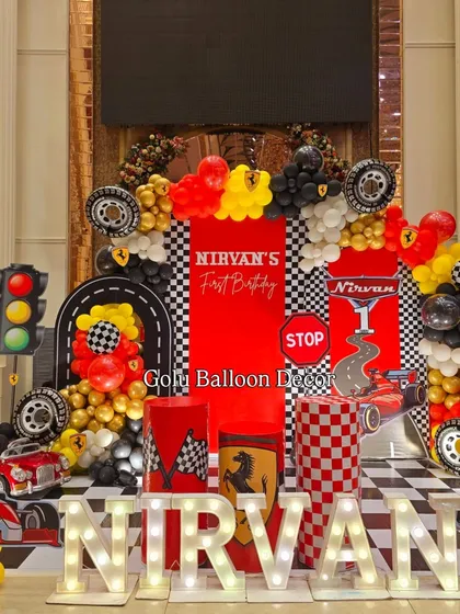 I bring high-octane fun with a Ferrari racing theme for a first birthday. This setup includes a custom backdrop with checkered flags and road signs, tire props, and the baby's name in bold marquee letters.
