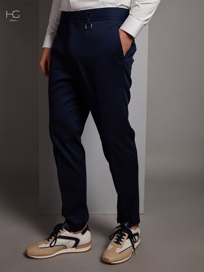 A full view of the tailored navy trousers, showing their clean lines and how they can be dressed down with sneakers for a modern look.