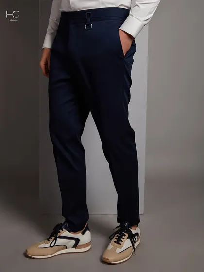 A full view of the tailored navy trousers, showing their clean lines and how they can be dressed down with sneakers for a modern look.