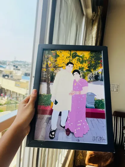 Holding up a freshly made illustrated portrait of a couple in traditional wear. The bright yellow background from the original photo makes the illustration pop, creating a vibrant and memorable keepsake.