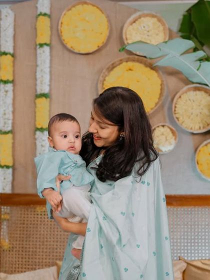 A tender moment between mother and child. The backdrop features traditional flower garlands and 'muram' filled with marigolds, adding a touch of authentic charm.