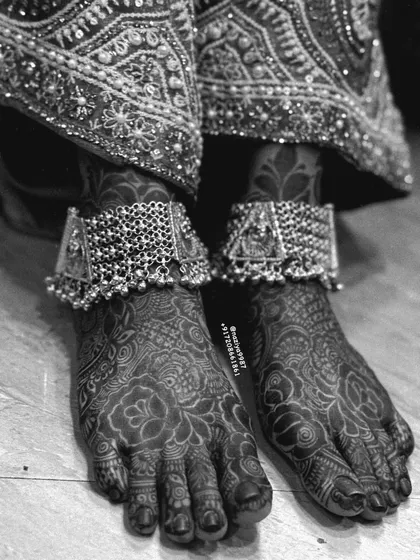 A black and white photo of a bride's feet, adorned with henna and payals.